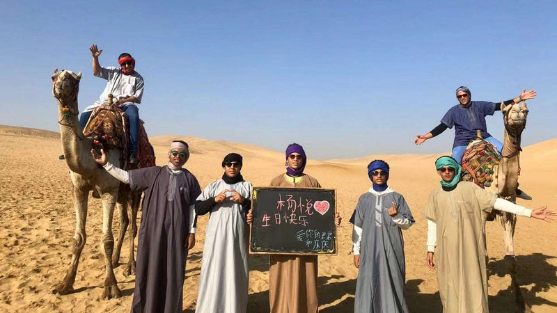 The Sahara filming team with camels and a greeting board in the desert